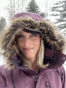 Picture of woman with blond hair wearing purple winter coat with a hood with fur on it